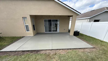 Newly poured residential broom finish concrete patio extension slab with clean tooled control joints in a backyard setting.