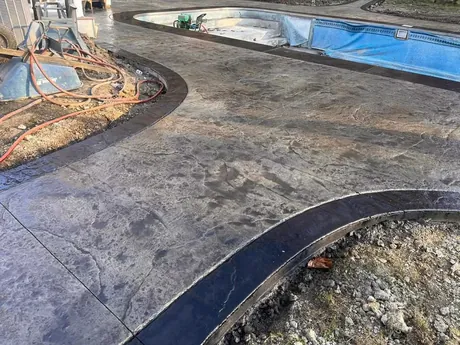 Decorative stamped concrete pool deck laid in a tile pattern around a residential swimming pool.