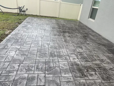 Grey ashlar stone stamped concrete patio with crisp grout lines beside a residential lawn.