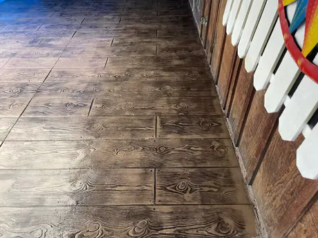Wood plank stamped concrete flooring in a warm brown tone, textured to read as timber boards.