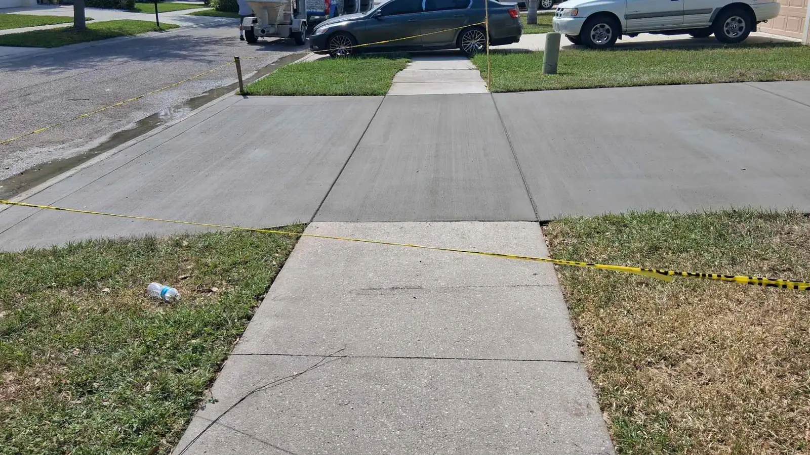 Newly poured grey broom finish concrete driveway apron and sidewalk section blocked off with yellow caution tape in a suburban residential neighbourhood.