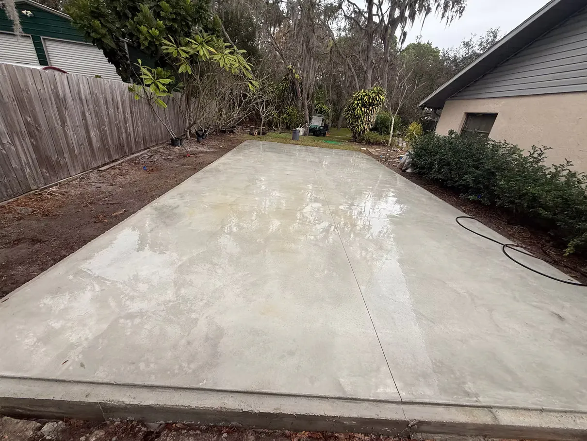 Freshly poured and floated concrete slab patio, still wet, formed square against a house wall.