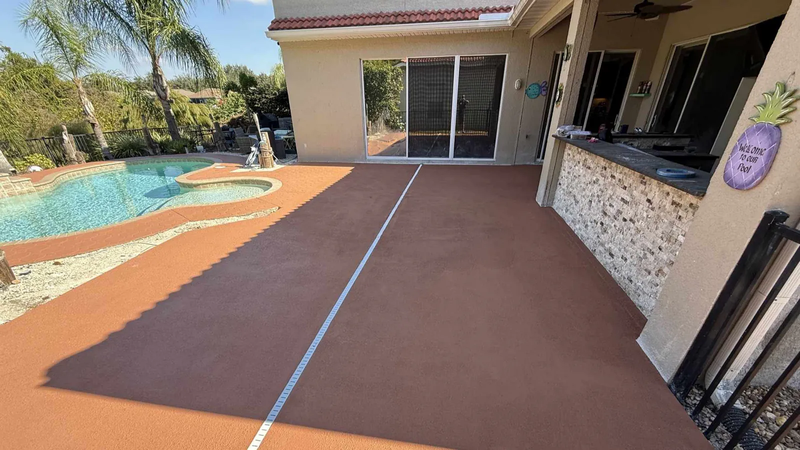 Terracotta brown knockdown finish concrete pool deck and patio overlay with an integrated white deck drain system next to an outdoor kitchen bar.