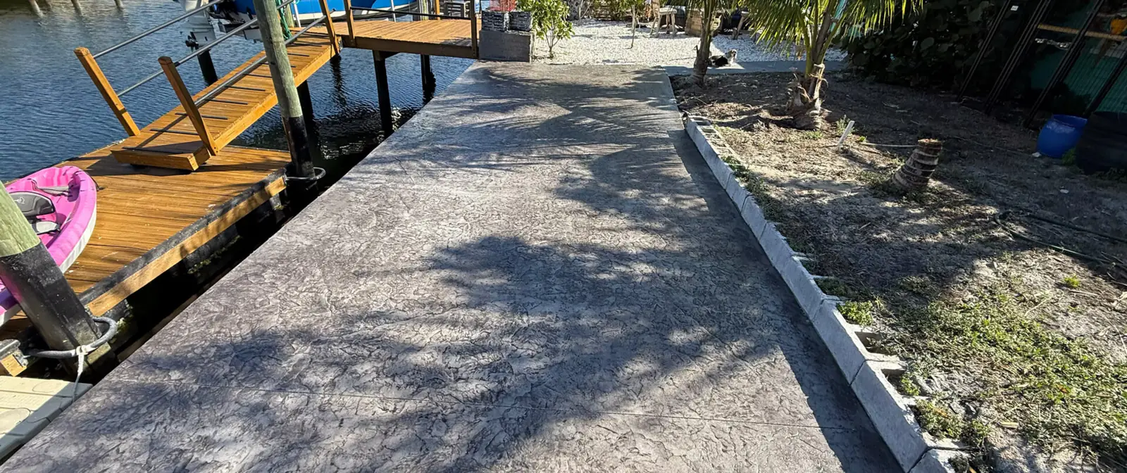 A stamped concrete walkway running out to a covered residential boat dock over the water.