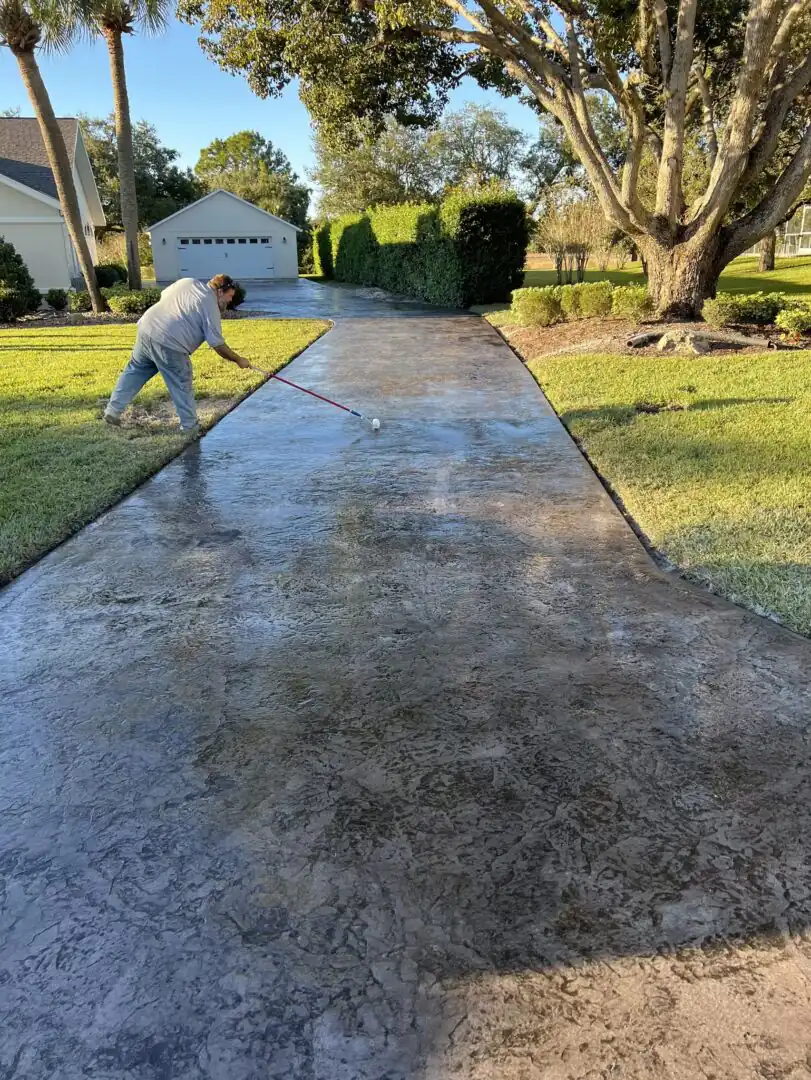 A stamped concrete driveway during resealing, the sealed section noticeably richer in colour than the unsealed one.